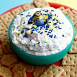 red plate with crackers, cookies with a blue bowl in the middle filled with white cookie dip with sprinkles and a minion figure