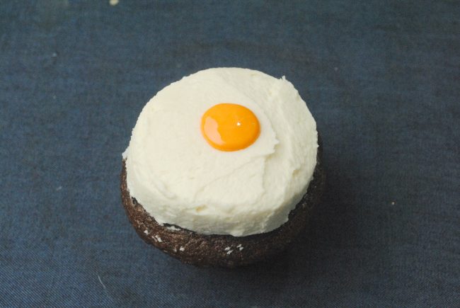 iced white cupcake with a yellow center for step two of the bloody eyeball cupcake recipe 