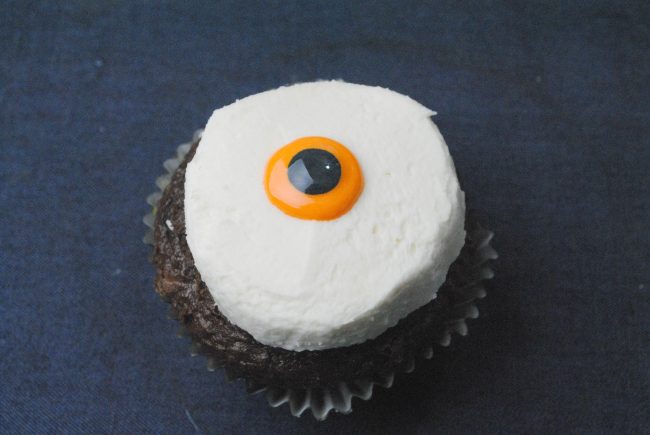 iced white cupcake with a yellow center with black pupil for step three of the bloody eyeball cupcake recipe 