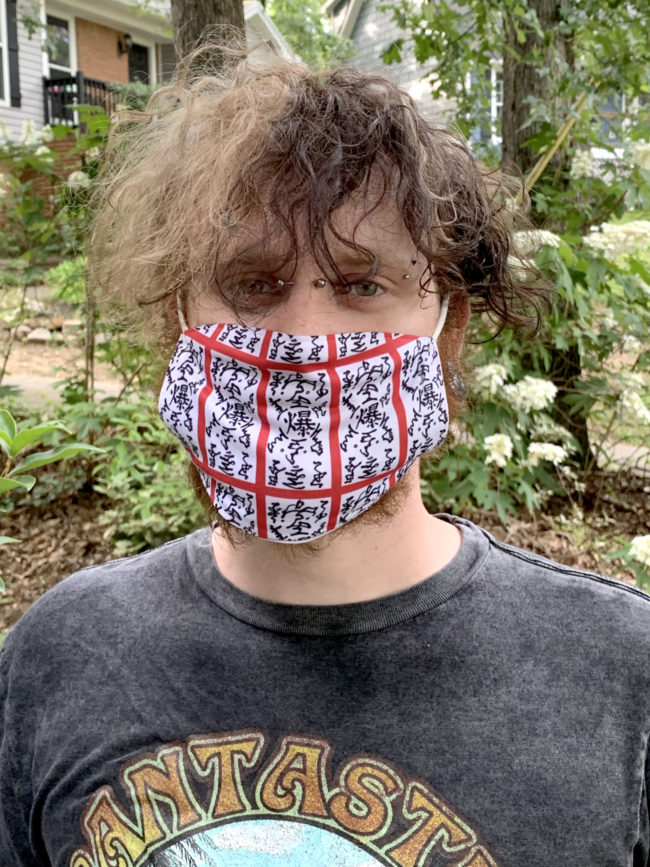 a teenager with dark hair wearing a black, red, and white mask featuring the Naruto paper bomb design gifts from redbubble 