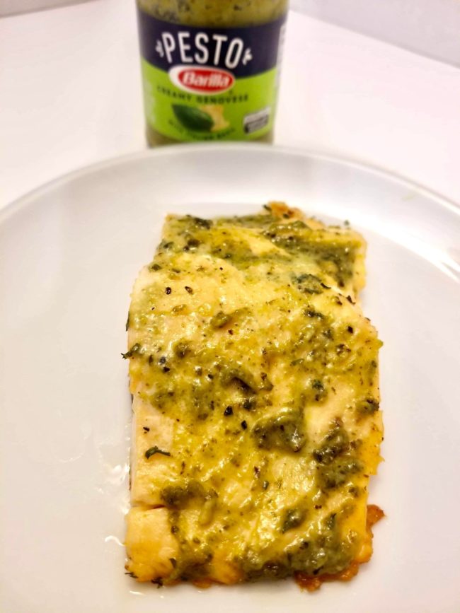pink atlantic salmon on a white plate covered in green genovese pesto sauce